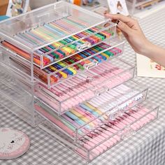 a clear drawer with many pens and pencils in it on a checkered table cloth