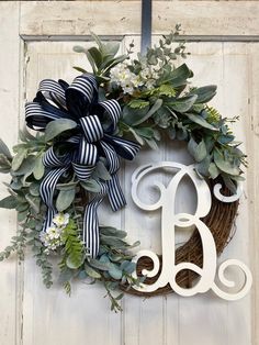 a wreath with the letter b on it is hanging on a door and decorated with greenery