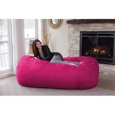 a woman sitting on a large pink bean bag chair in front of a fire place