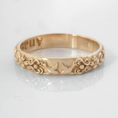 a gold wedding ring with an ornate design on it's side and the word happily written in cursive writing