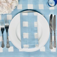 a place setting with silverware and flowers on a blue checkered cloth tablecloth