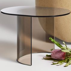 a glass table with a flower on it next to a round object that looks like a vase