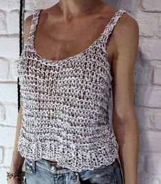 a woman standing next to a brick wall wearing a tank top with crochet