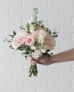 a person holding a bouquet of pink and white flowers with greenery in their hands