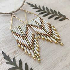 a pair of white and gold beaded earrings hanging from a string on a wooden table