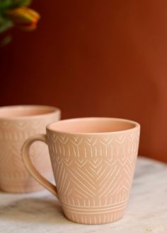 two mugs sitting on top of a table next to a vase with flowers in it