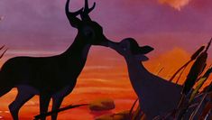 two deer standing next to each other in front of an orange and purple sky with clouds