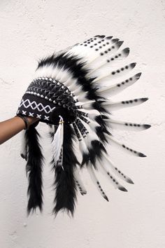 a person is holding up a black and white feather headdress on a wall