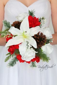 a bride holding a red and white bouquet with pine cones on the bottom, while wearing a strapless wedding dress