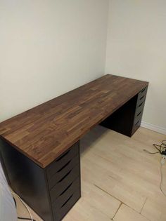 a wooden desk with drawers in an empty room next to a white wall and hard wood floor