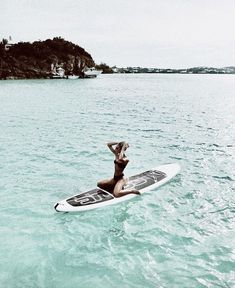 a person laying on a surfboard in the middle of the ocean with an island in the background