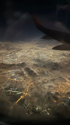 an aerial view of the city lights and clouds at night as seen from an airplane