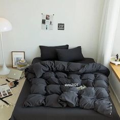 an unmade bed in a white room with black sheets and pillows on the floor