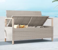 a wicker storage bench with cushions on the top and bottom, in front of a white wall