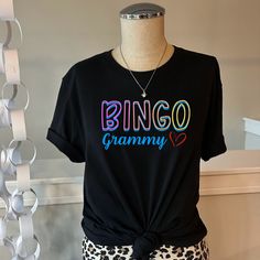 Hello, and thank you for stopping by!  Are you looking for a perfect gift for the Bingo lover in your life? Do you want to show off at the Bingo hall next week? Our Bingo collection has something special for Bingo players everywhere!  This one is for all the Grammy's.  Unisex T-shirts that are so soft and comfy. You'll want to live in them!  FABRICATION * Solid Colors: 100% Ringspun Cotton * Heather Colors: 52% cotton, 48% polyester * Runs true to size *For oversized look, size up one to two sizes from your usual size SIZING This style is a unisex t-shirt. If you are unsure about the size you should order, please refer to the size chart in the pictures. CARE INSTRUCTIONS * Machine wash: warm (max 40C or 105F) * Tumble dry: low heat * Do not iron directly on print * Do not dry-clean We aim Bingo Lover Gift Ideas, Multicolor Letter Print Tops As Gift, Multicolor Text Print Tops As Gift, Multicolor Text Print Top As Gift, Multicolor Text Print Top As A Gift, Fun Black Tops As Gift, Fun Black Top As Gift, Fun Black T-shirt As A Gift, Multicolor Graphic Tee T-shirt As Gift