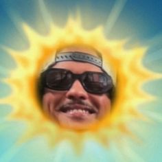 a man wearing sunglasses and smiling in front of a sunburst with his eyes closed