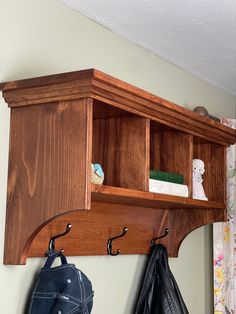 a wooden shelf with two coats hanging from it's sides and a purse on the other side