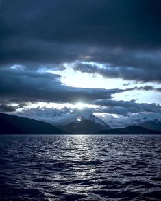 the sun shining through clouds over water with mountains in the background