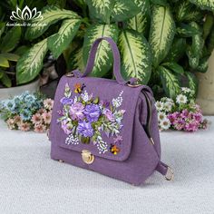 a purple handbag with flowers on it sitting in front of some potted plants