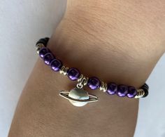 Black and purple pearlescent beads with a Saturn pendant. Adjustable Nickel-free Purple Charm Bracelet, Purple Pearl Bracelet As Gift, Adjustable Purple Pearl Bracelet Gift, Adjustable Purple Pearl Bracelet As Gift, Saturn Bracelet, Saturn Jewelry, Ohm Jewelry, Planet Bracelet, Pulseras Aesthetic