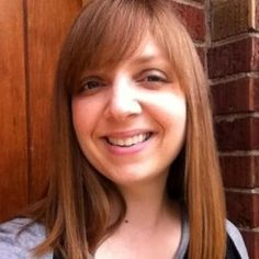 a woman standing in front of a brick wall smiling at the camera with long hair