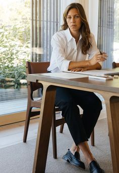 a woman sitting at a table with a book and pen in her hand while looking off to the side