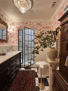 the bathroom is decorated with pink and white wallpaper, black cabinetry, and an ornate chandelier