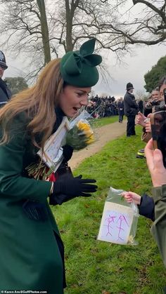 a woman in a green dress and hat is handing flowers to another woman with her hand