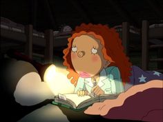 a woman sitting in bed reading a book with a light shining on her face and red hair