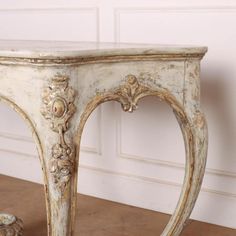 an old white console table with carvings on the top and bottom, sitting against a wall