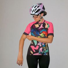 a woman wearing a colorful shirt and bicycle helmet looking at her cell phone while standing in front of a gray background