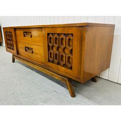 a wooden sideboard with carved designs on the front and sides, sitting against a white wall