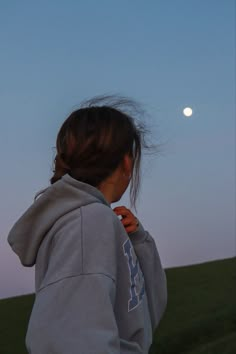 a girl in a hoodie looking at the moon