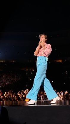 a man in blue pants and pink shirt walking on stage with his hands clasped to his face