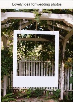 a wedding sign hanging from the side of a white arbor with greenery around it