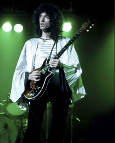 a man with long hair holding a guitar in front of some green lights on stage