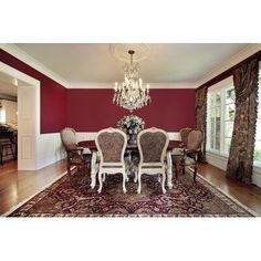 a formal dining room with red walls and white chairs, chandelier and rug