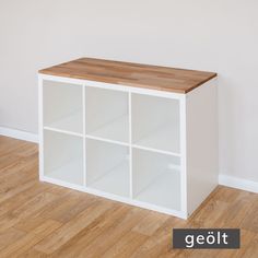 a white bookcase with wooden top in front of a wall and hardwood flooring