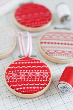 three red and white embroidered coasters on a table with sewing thread, spooling and scissors