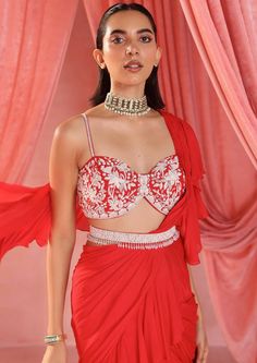 Embellished choli paired with a pre-stitched ruffle sari and embellished belt with tassels. Red Embellished Pre-draped Saree For Party, Red Embellished Pre-draped Saree, Elegant Red Embellished Pre-draped Saree, Red Hand Embellished Choli, Hand Embellished Red Choli, Red Pre-draped Saree With Mirror Work For Evening, Designer Red Party Set, Glamorous Evening Choli With Cutdana Detailing, Glamorous Evening Choli With Cutdana