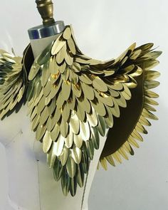 a white mannequin with gold leaves on it's chest and wings around the neck