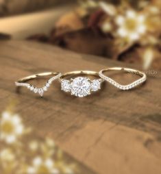 three different types of wedding rings on a wooden surface with flowers in the back ground