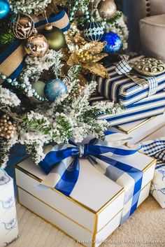 a christmas tree with presents under it and blue and gold ornaments on the trees branches