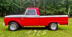 an old red pick up truck parked in the grass with trees in the back ground