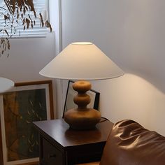 a lamp sitting on top of a wooden table next to a brown leather couch in front of a window