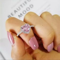 a woman's hand holding a ring with a pink heart shaped diamond on it