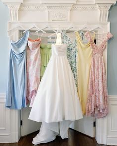 there are many dresses hanging up on the rack in front of a fireplace mantel