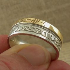 Sterling Silver and 10K Yellow Gold with Claddagh and Celtic Knot Design around the entire ring. A custom personalized phrase in Ogham on 10K yellow rail edge. Claddagh & Celtic Knot Wedding Band with Ogham Script Rail. Handmade in Ireland. 7.5 mm wide. Available in whole & half Sizes 4.5 to 13. Florentine background with polished design, your personalized phrase in Ogham Script on rail edge. Comfort Fit. Irish Hallmark. The phrase is usually a name or word or short phrase. Start a conve Unique Engraved Wedding Jewelry, Unique Engraved Jewelry For Wedding, Symbolic Yellow Gold Engraved Wedding Ring, Symbolic Engraved Yellow Gold Ring For Wedding, Symbolic Yellow Gold Engraved Ring For Wedding, Ceremonial Silver Engraved Ring Stamped 14k, Ceremonial Silver Engraved Ring, Stamped 14k, Symbolic Engraved Ring With Intricate Design For Anniversary, Symbolic Engraved Wedding Ring With Engraving Option