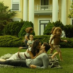 a man and woman laying on top of a blanket in front of a yellow house