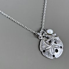 Small Sand Dollar Necklace - This is a smaller version of my other Sand Dollar necklace. The Sand Dollar is accented with a a Silver Pewter Starfish and White Freshwater Pearl. The Sand Dollar is approximately 17mm (slightly smaller than an US dime) and has a hollow back. Stainless Steel Chain For other Sand Dollar Necklaces: https://www.etsy.com/shop/mcstoneworks?search_query=sand+dollar+necklace Silver Sand Dollar Necklace, Sand Dollar Jewelry, Silver Charm Necklace For Beach, Silver Charm Necklaces For Beach, Ocean-inspired Strand Jewelry With Starfish Charm, Ocean-inspired Silver Jewelry For Wedding, Silver Starfish Jewelry For Vacation, Silver Strand Shell Necklace For Beach, Beachy Silver Strand Jewelry